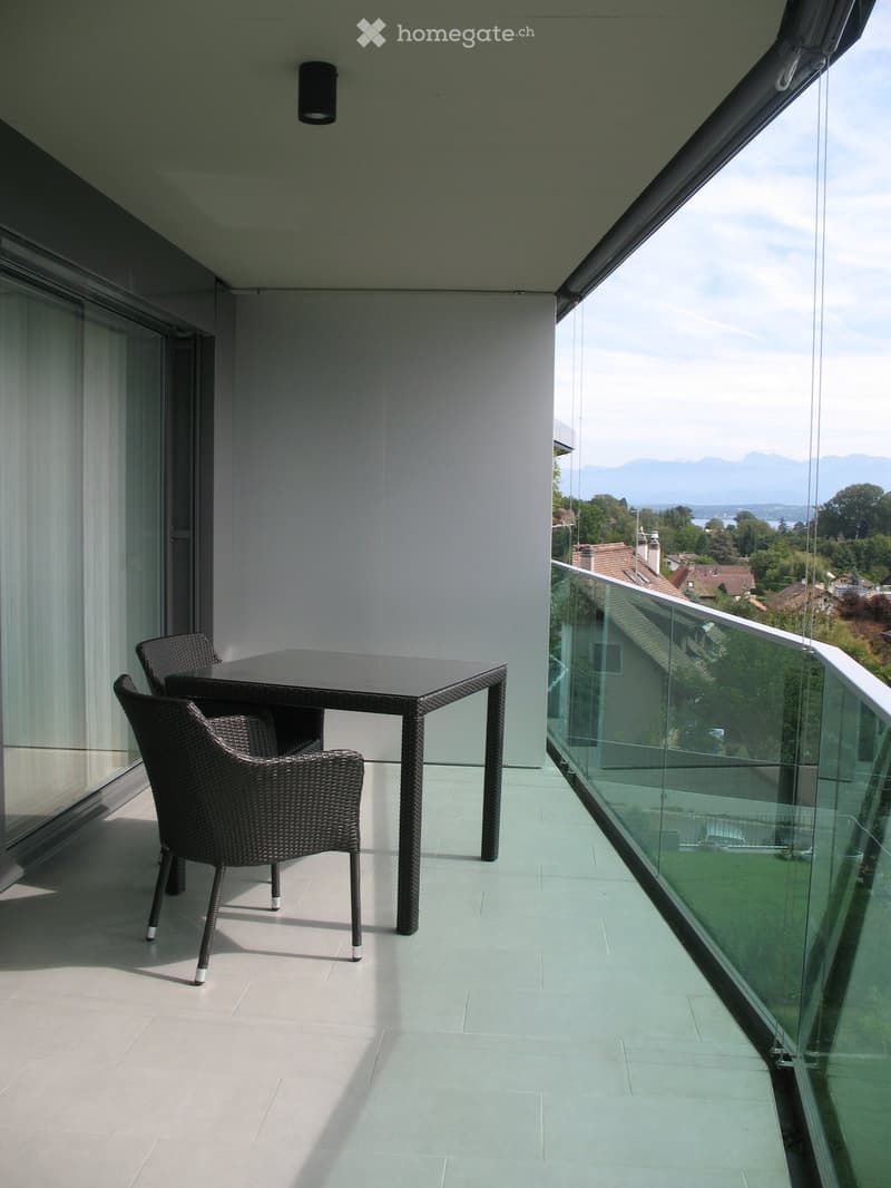 modern balcony, glass railings, table with two chairs, white tiled floor, outdoor lighting, scenic view