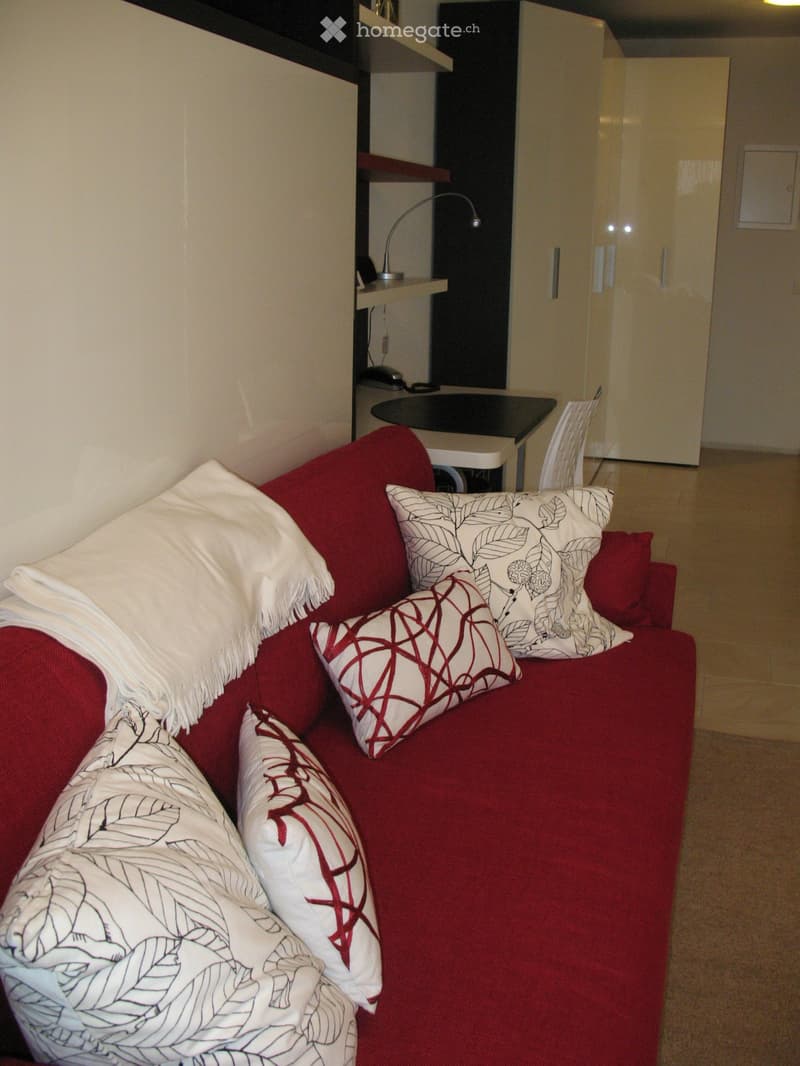 Red sofa with four pillows, small table with chair, lamp, cabinets in the background