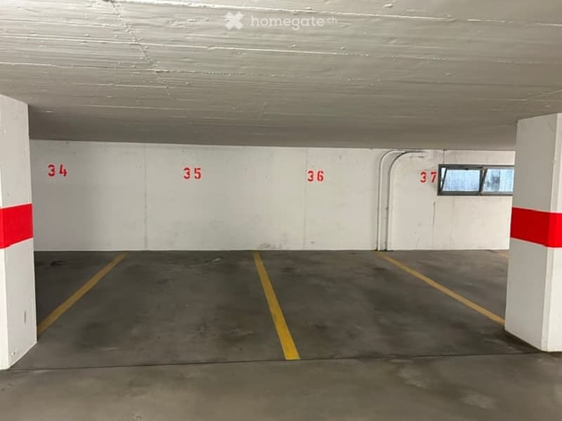 Underground parking area with numbered parking spaces, white pillars, and yellow floor markings.
