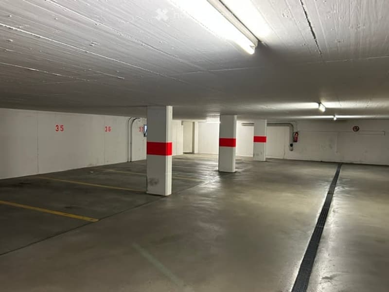 Underground parking area with numbered spaces, concrete pillars, and fluorescent lighting.