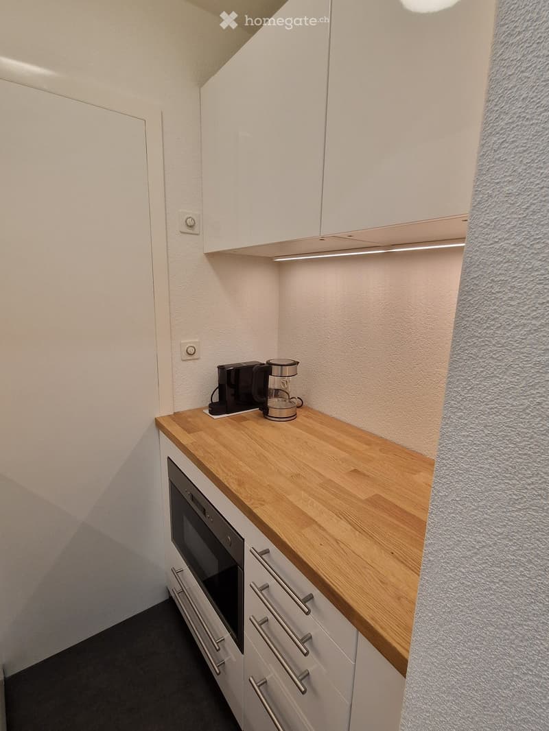Compact kitchen with white cabinets, wooden countertop, built-in oven, and coffee maker on the counter.