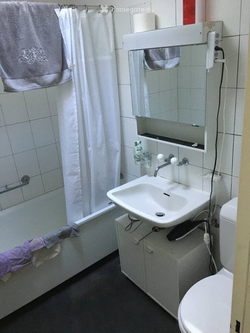A small bathroom with a white sink, toilet, bathtub, and mirror. Towels are hanging on the wall, and a cup is placed on the sink counter.