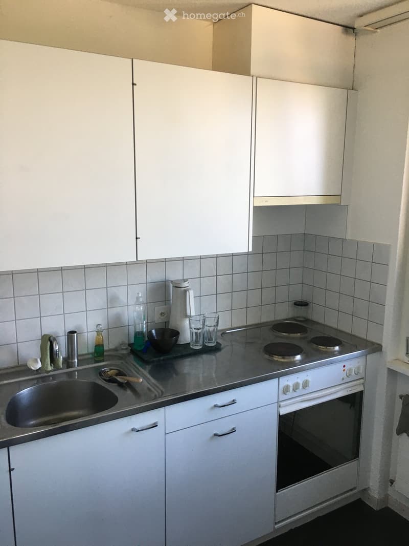 A small kitchen with white cabinets, a stainless steel sink, a four-burner electric stove, and various small appliances and items on the counter.