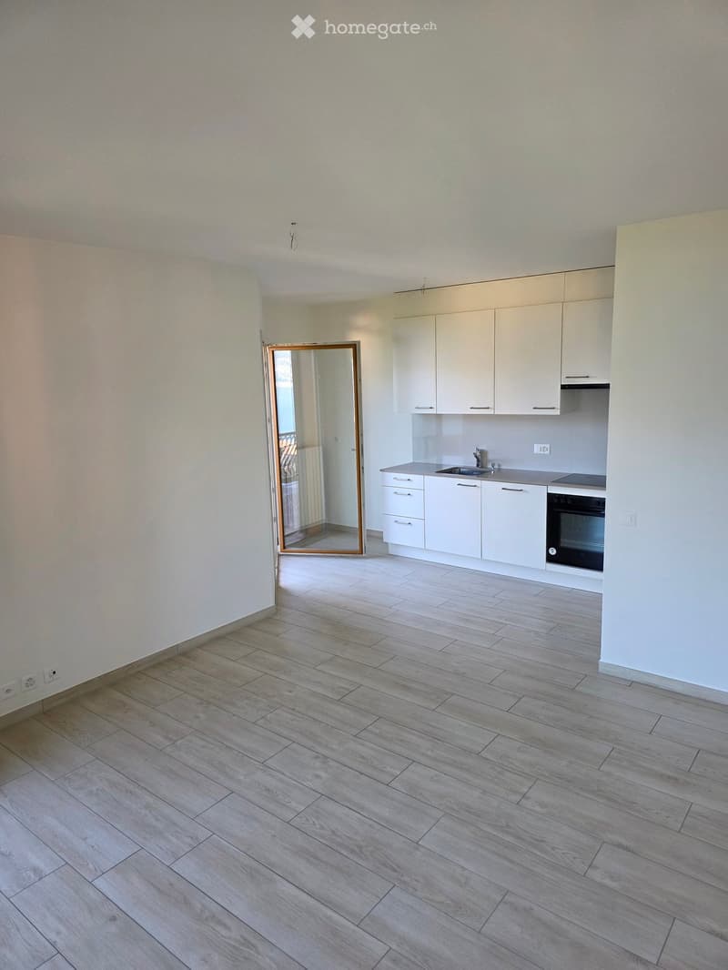 Empty kitchen with white cabinets, a sink, and a stove, featuring light wooden flooring and a large mirror on the wall.