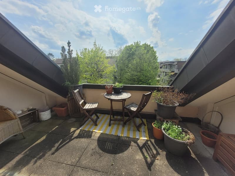Balcony with a small table, two chairs, a wicker chair, and several potted plants.