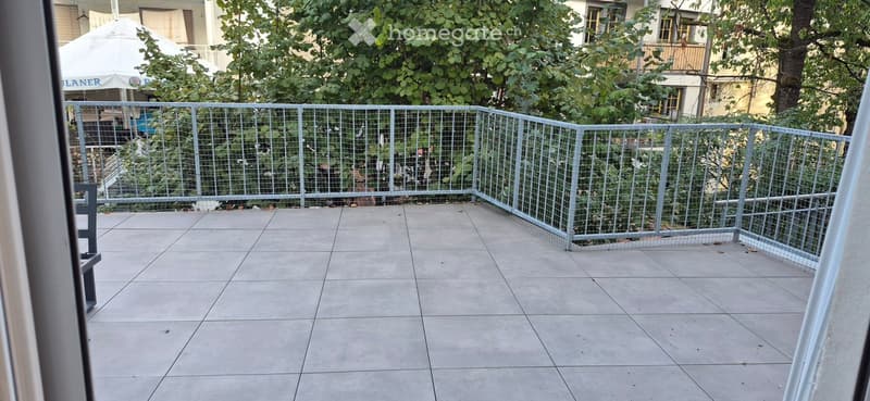 Balcony with tiled floor, metal railing, and greenery visible beyond the railing.