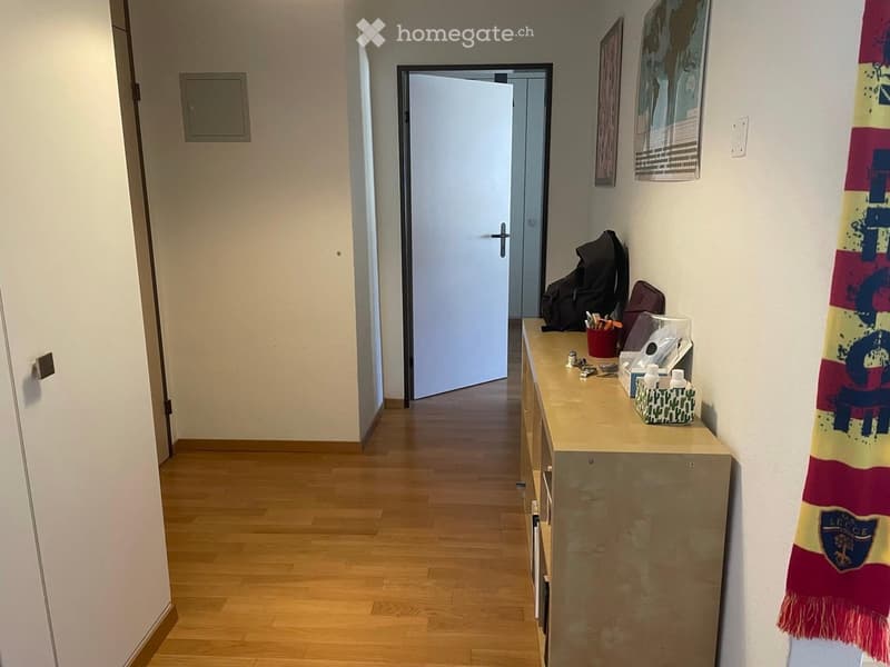 Hallway with wooden flooring, a small table with personal items, and a door leading to another room.