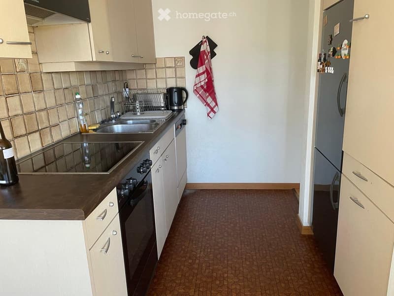 Modern kitchen with white cabinets, dark wooden countertop, stainless steel sink, oven, and refrigerator. Beige tiled backsplash and wooden flooring.