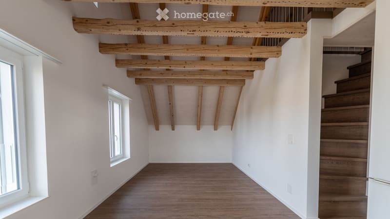 Empty hallway with exposed wooden beams on the ceiling, wooden flooring, and a staircase leading upwards.