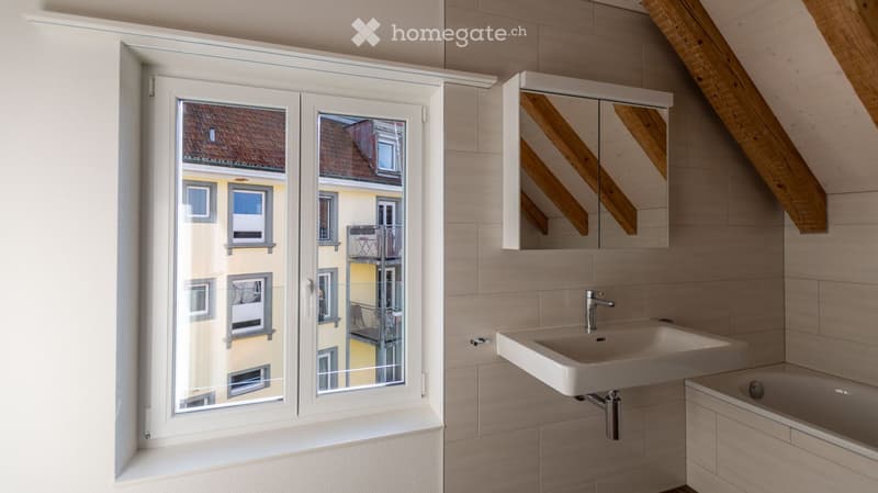 Modern bathroom with a large window offering a view of a neighboring building, a white sink, a bathtub, and a mirrored cabinet.