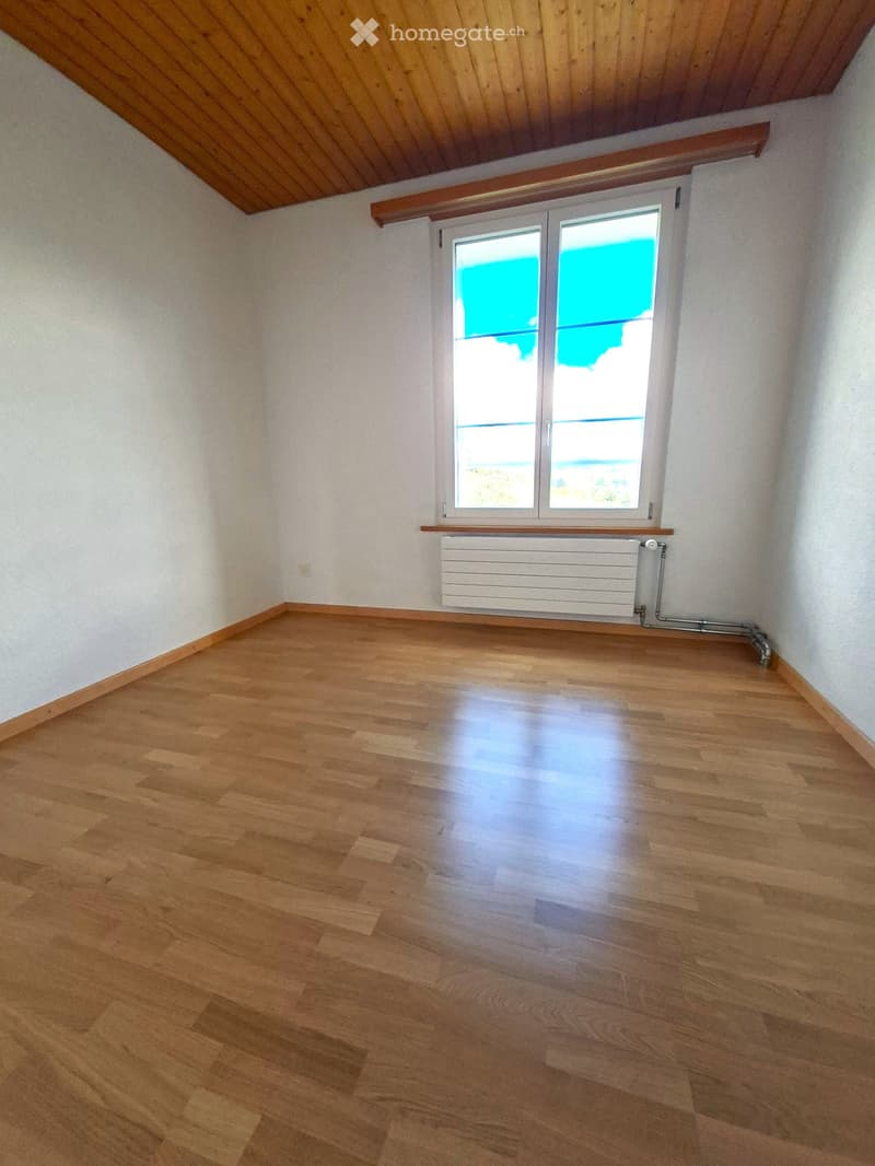Empty room with wooden flooring, white walls, and a large window with a view of the outdoors. A radiator is mounted below the window.