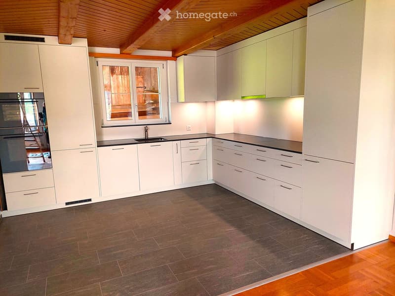 Modern kitchen with white cabinets, dark countertops, and a wooden floor. Features an oven, sink, and ample storage space.