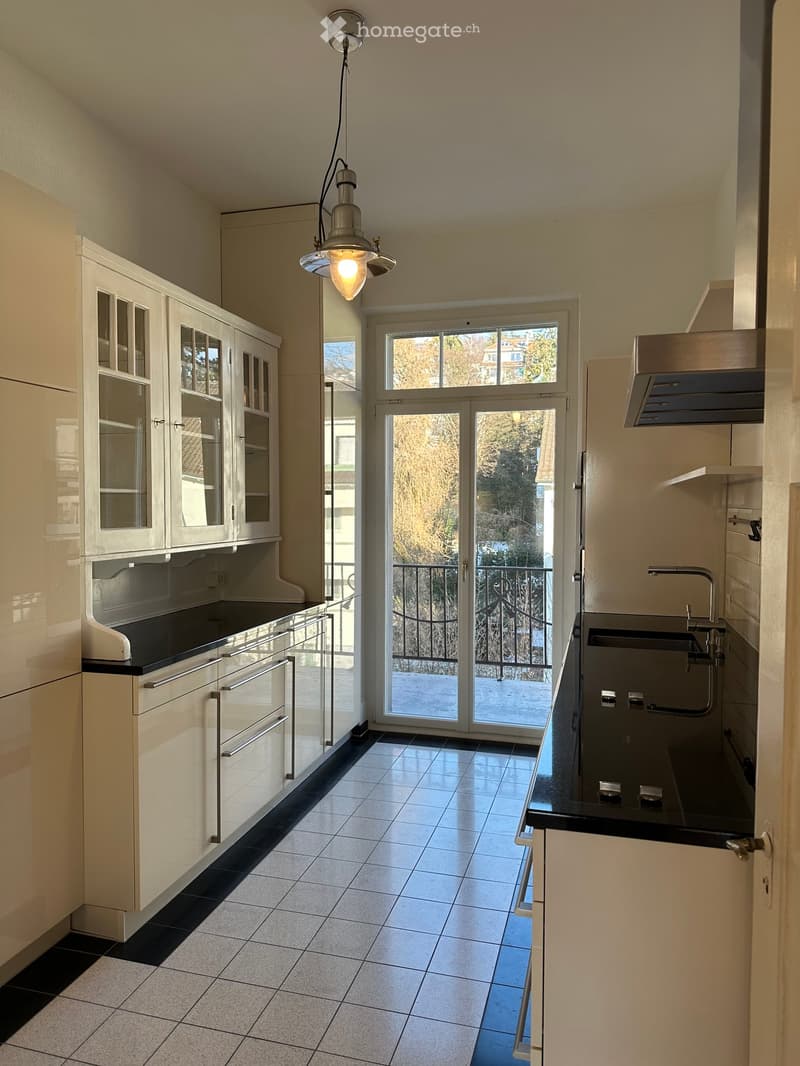 modern kitchen with tile flooring, white cabinets, black countertop, sliding glass door to balcony, stainless steel faucet, stainless steel sink, lamp