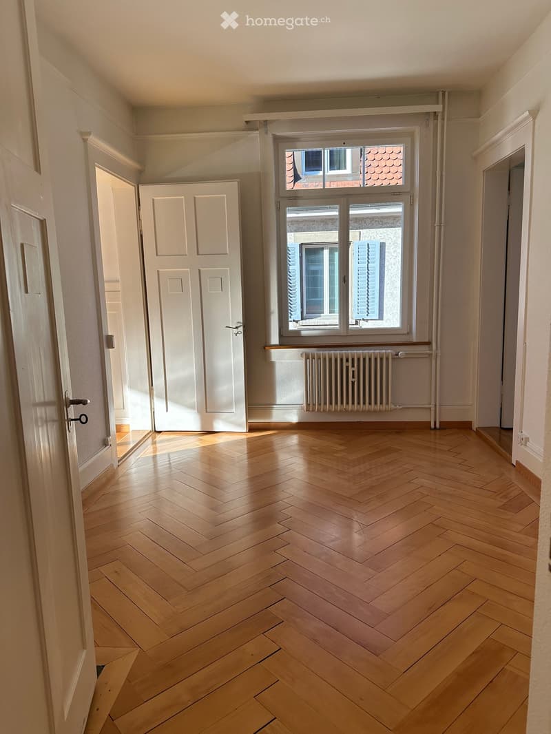 empty room, wooden parquet floor, large window, radiator, two doors