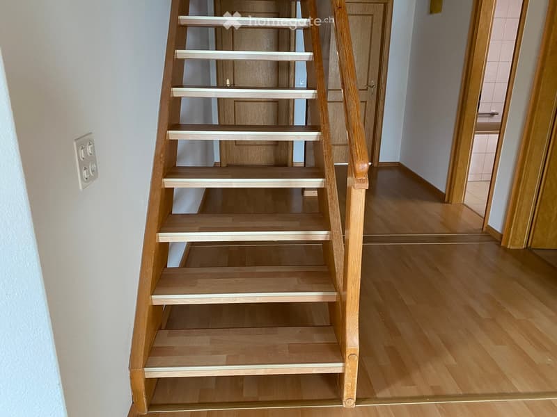 Wooden staircase with white handrails leading to an adjacent room with wooden flooring and a door.