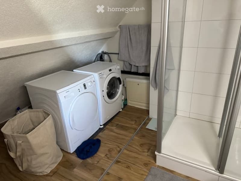 Compact bathroom with a washing machine and dryer unit, a glass-enclosed shower, and a towel hanging on the wall.