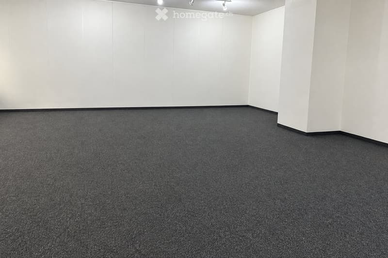 Completely empty room with bare white walls and dark grey carpeted floor. No furniture or equipment.