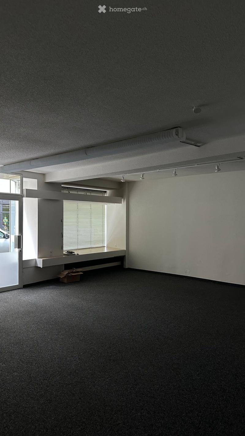 Empty room with grey carpeted floor, white walls, and a small built-in bench with a window and blinds. No furniture or equipment.