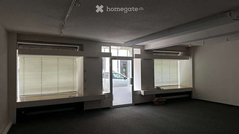 Empty room with carpeted floor, large windows with blinds, and a door leading outside. No furniture or equipment present.