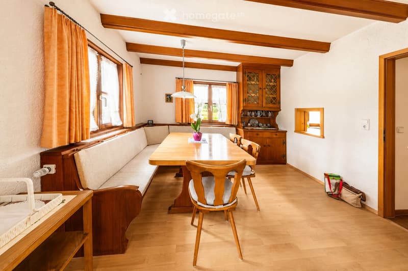 Cozy dining area with wooden furniture, a long bench sofa, a dining table with chairs, and a cabinet with glass doors.