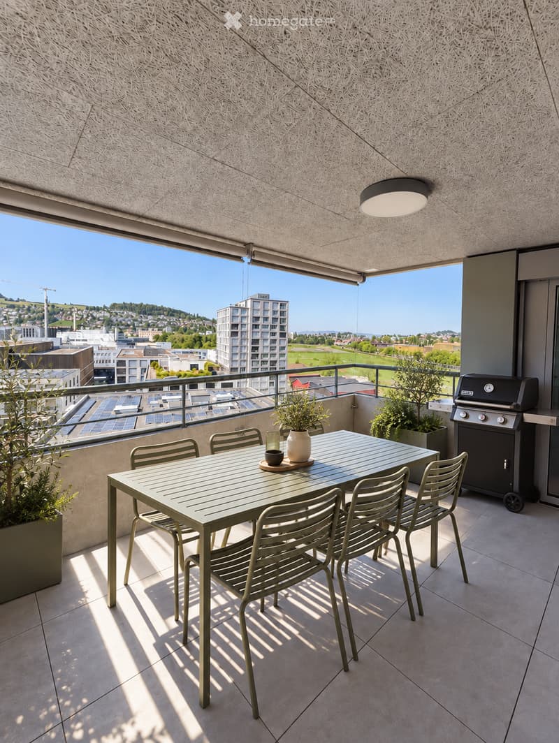 Balcony with a modern dining setup, including a table, chairs, a vase, and a grill, overlooking a cityscape with buildings and greenery.