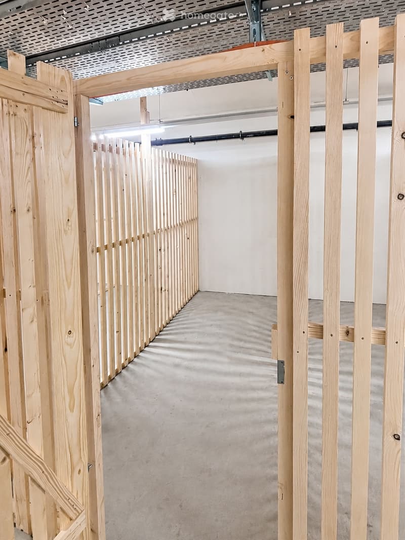 Empty hallway with unfinished wooden walls and a concrete floor, featuring exposed construction elements and lighting fixtures.