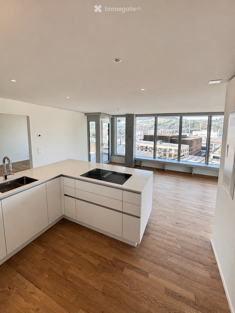 Modern kitchen with white cabinets, wooden flooring, and large windows offering a city view. Features a sink, faucet, and countertop.