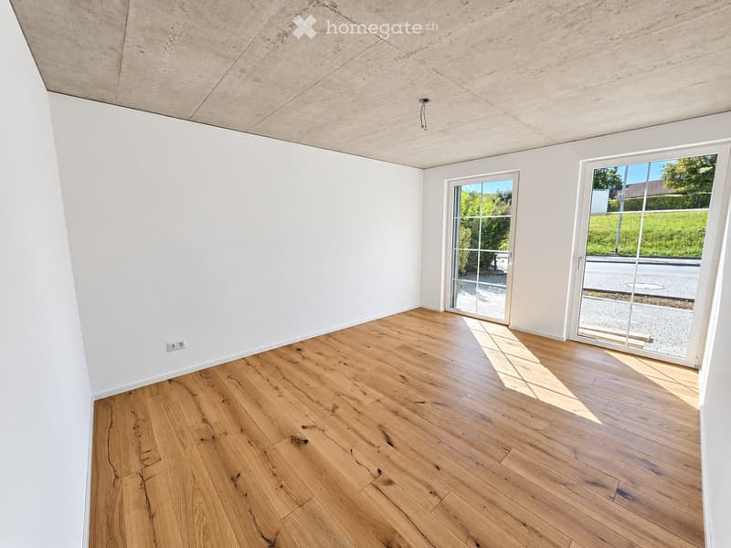 Empty room with light wooden flooring, white walls, and large glass doors leading to an outdoor area.
