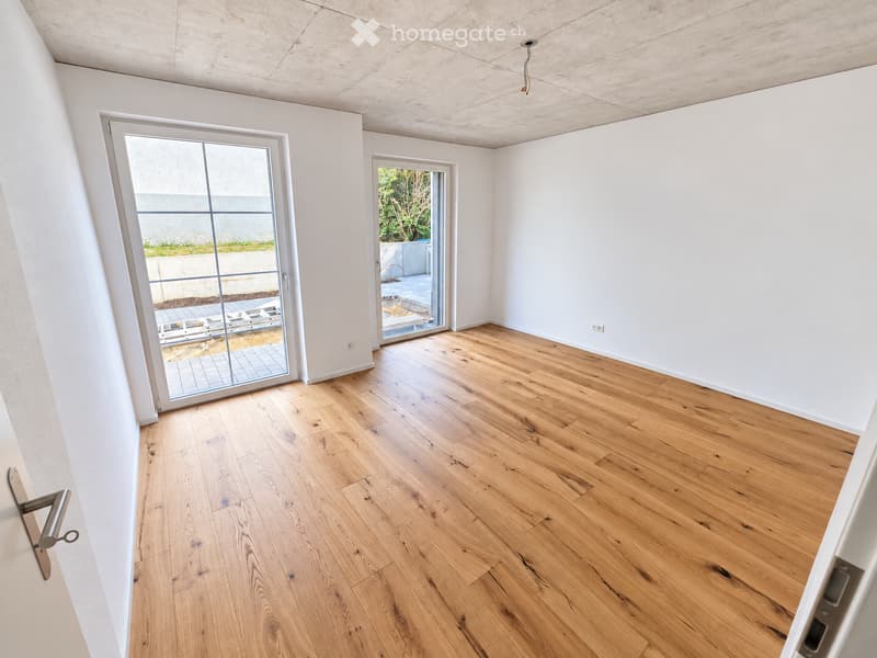 Empty room with light wooden flooring, white walls, and large glass sliding doors leading to an outdoor area.