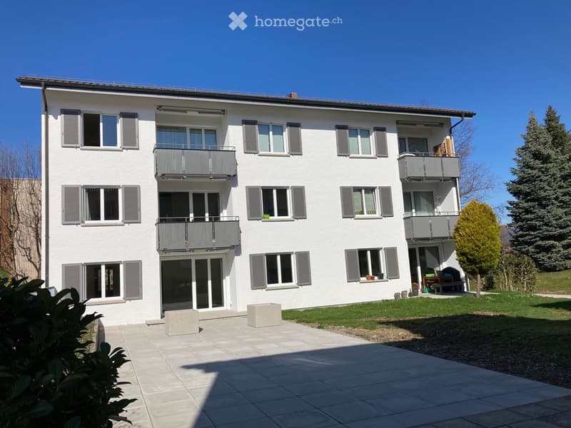 White building, multiple balconies, large windows, paved driveway, trees and grass in the front