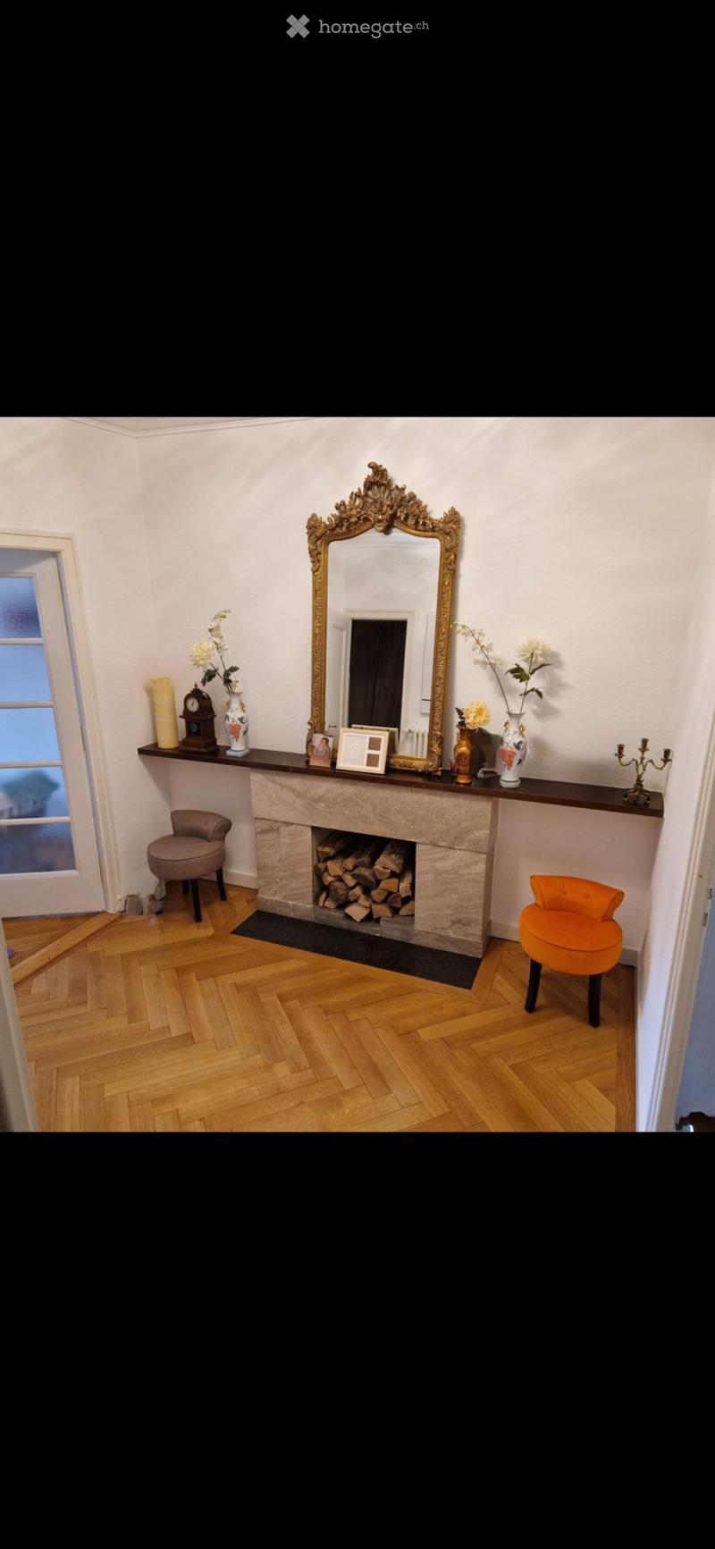 Elegant room with a stone fireplace, two colorful stools, a large ornate mirror, and decorative items on the mantelpiece.