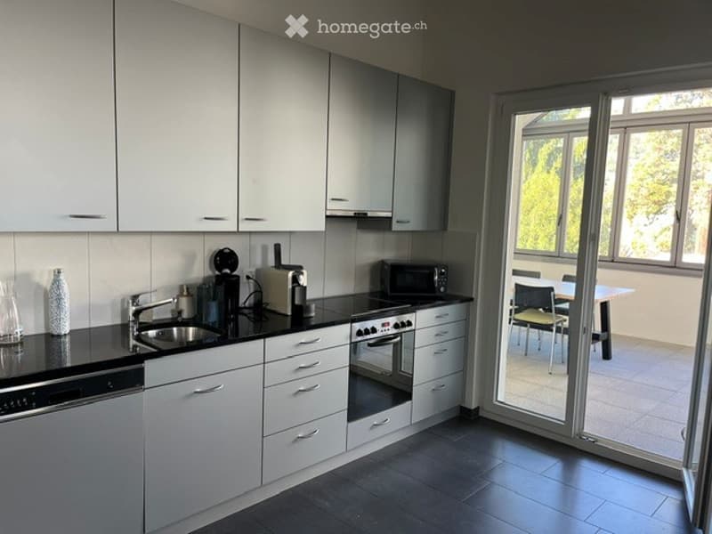 Modern kitchen with white cabinets, black countertops, and stainless steel appliances. Features a sink, oven, microwave, and dishwasher. A sliding glass door leads to a patio with a table and chairs.