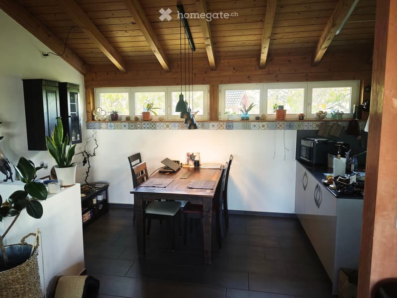 Open-plan kitchen and dining area with wooden beams, dark tiled floor, and modern kitchen appliances.