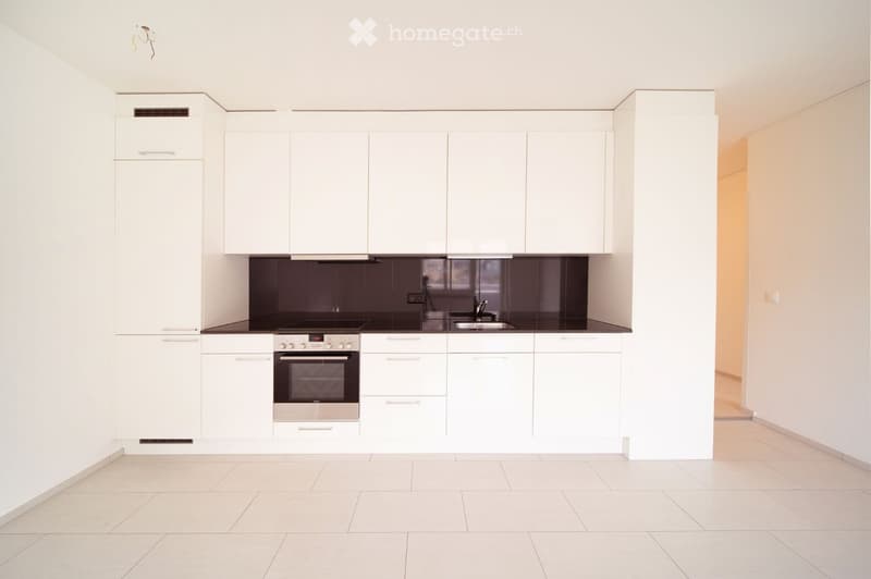 Modern kitchen with white cabinets, stainless steel oven, and sink, featuring a dark countertop and tiled floor.