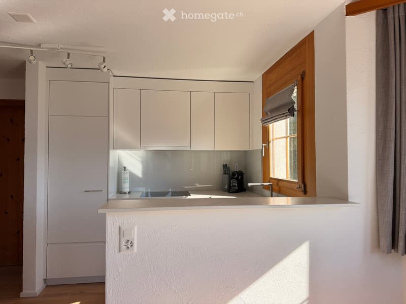 Modern kitchen with white cabinets, a central island, and a window with wooden frame and grey roller shade. Features a coffee maker, knife block, and sleek sink.
