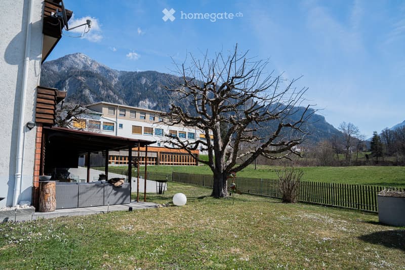 Outdoor patio area with a covered seating space, a tree, and a view of mountains in the background.