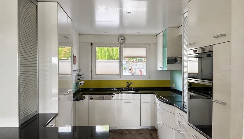 Modern kitchen with white cabinets, black countertops, stainless steel appliances, and a window view of greenery.