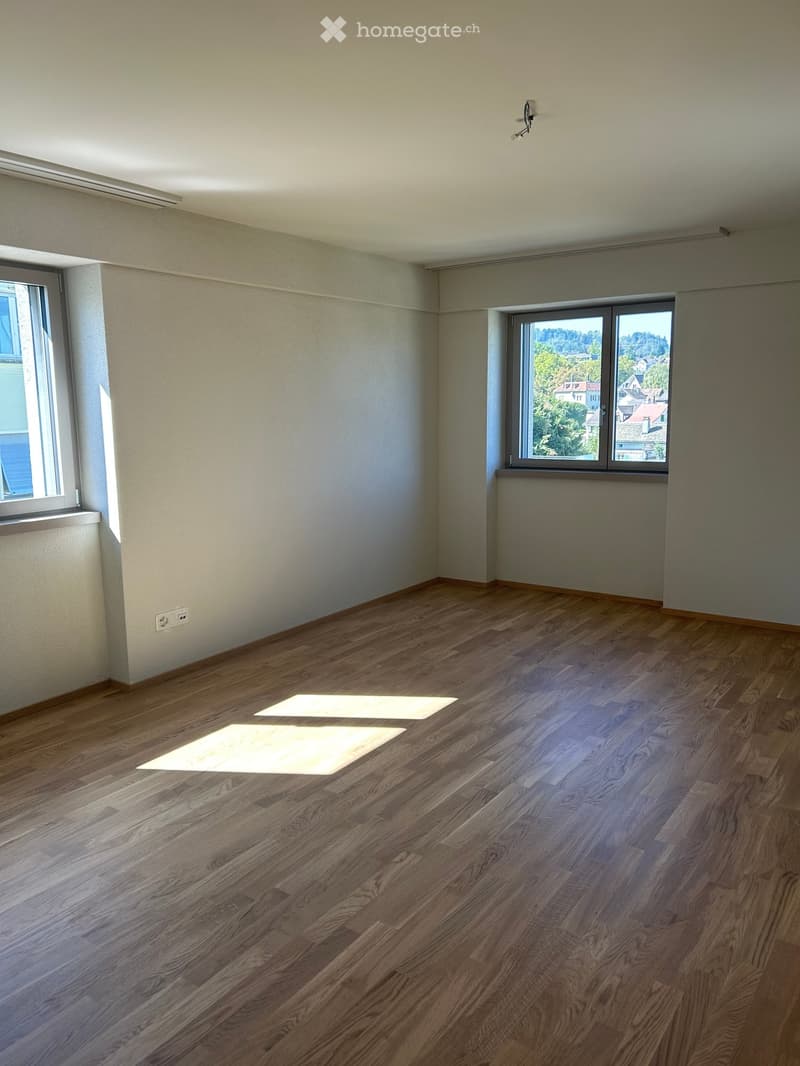 Empty room with wooden flooring, large windows, and natural light. No furniture or equipment present.