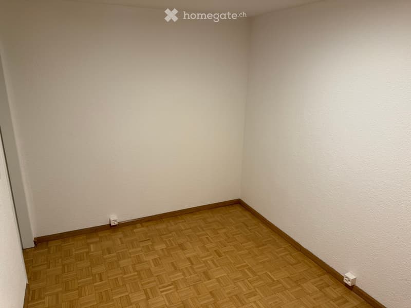 Empty room with light-colored walls and wooden herringbone flooring. No furniture or equipment visible.