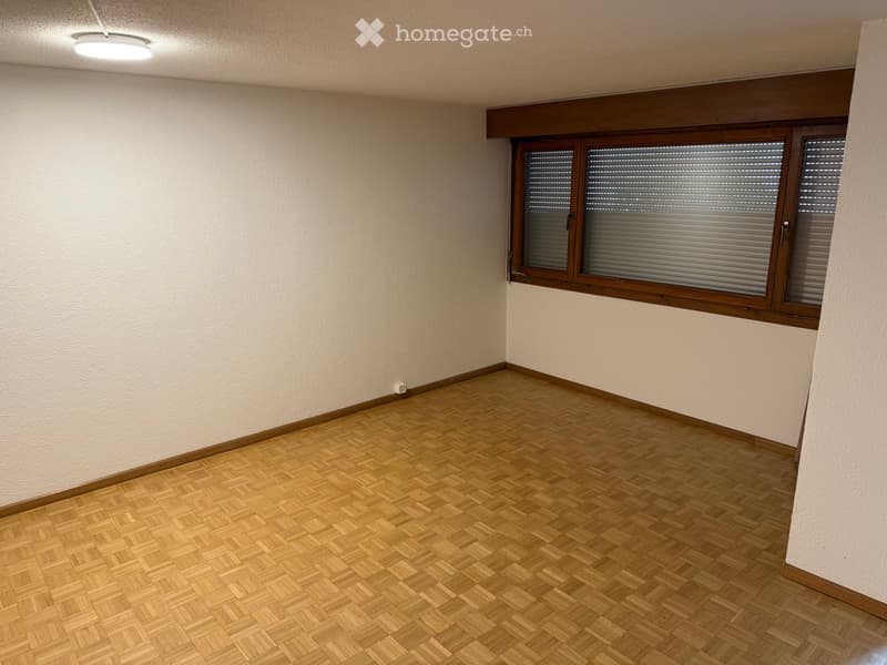 Empty room with wooden parquet flooring, white walls, and large windows with blinds.