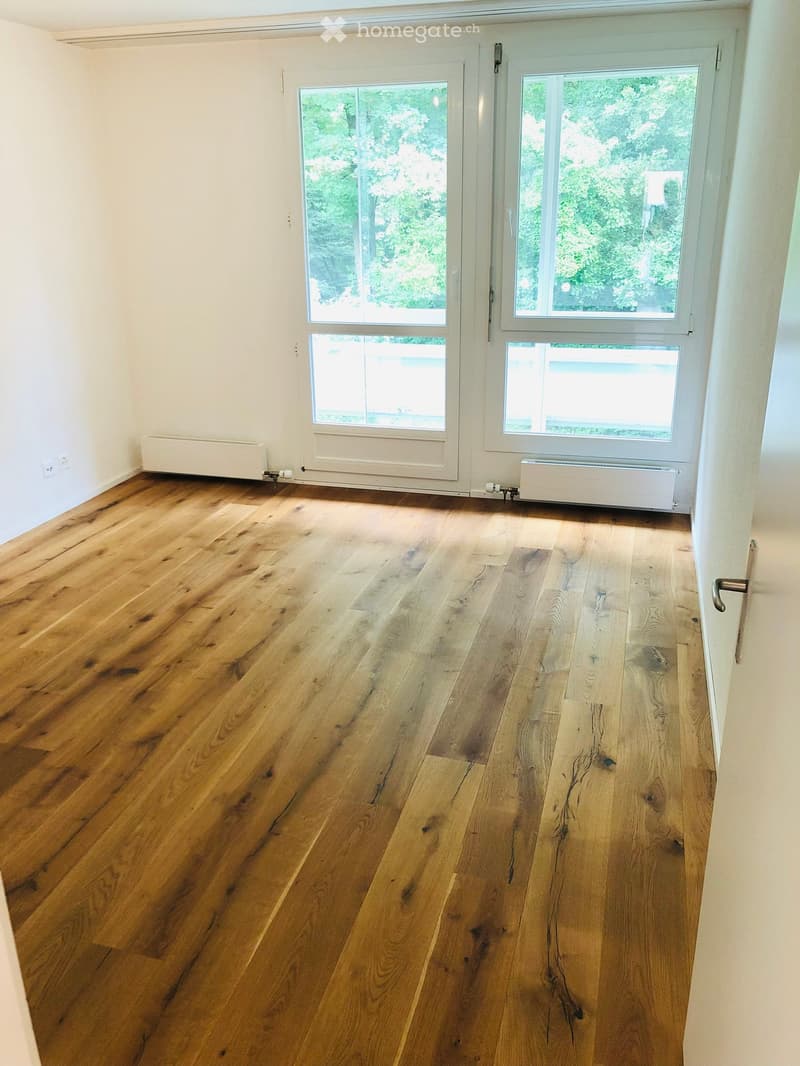 Empty room with wooden flooring, white walls, large windows, and radiators.