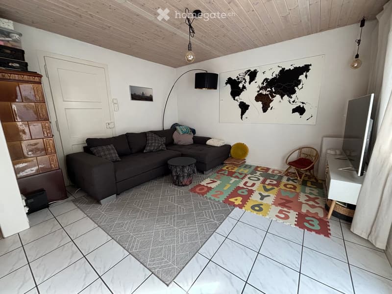 Living room with a dark grey sectional sofa, coffee table, wicker chair, TV stand, floor lamp, world map, and picture frame.