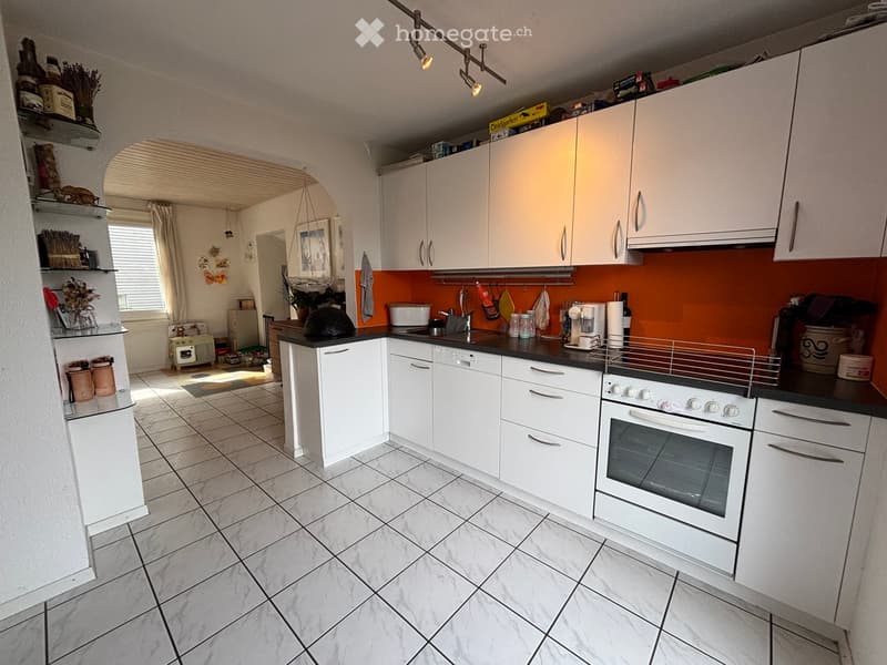 Modern kitchen with white cabinets, black countertops, and a bright orange backsplash. Features include an oven, dishwasher, coffee maker, and various kitchen utensils.