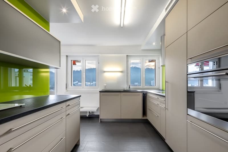 Modern kitchen with white cabinets, black countertops, stainless steel appliances, and large windows offering a scenic view.