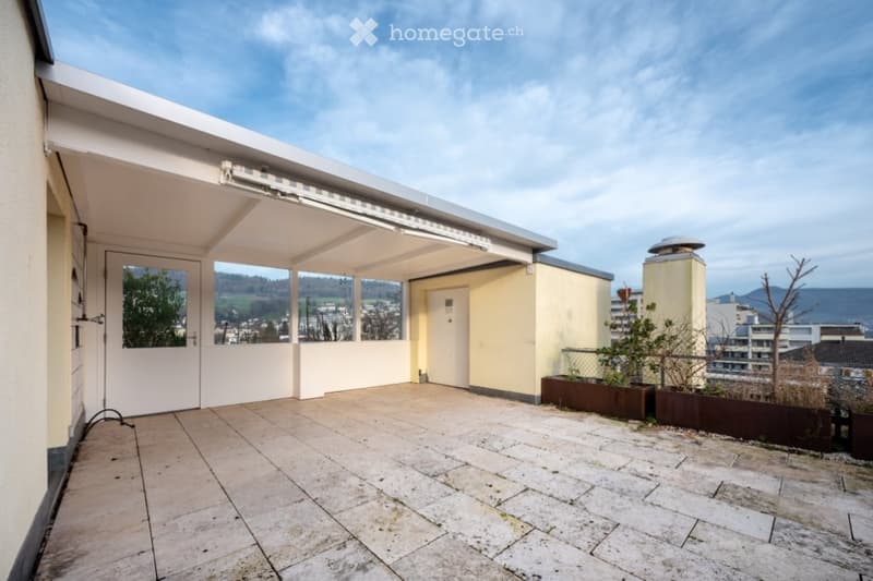 Roof terrace with tiled flooring, covered section, glass railings, and scenic view of the valley and cityscape.