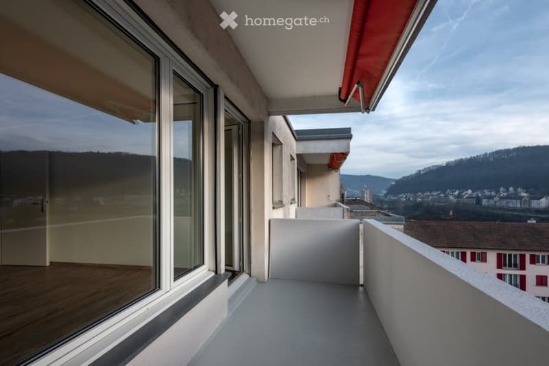 Modern balcony with large glass windows, wooden flooring, and a scenic view of the city and surrounding hills.