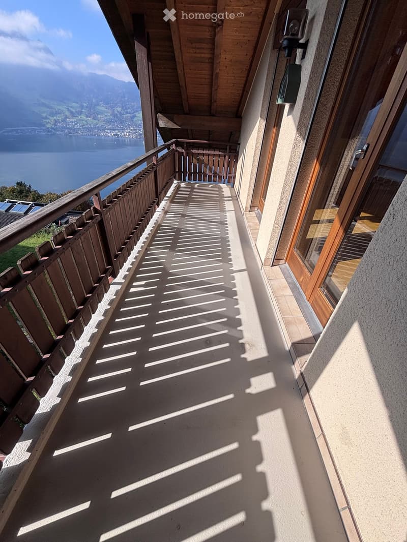 Balcony with wooden railing, tiled floor, and scenic mountain and lake view in the background.