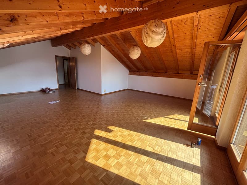 Empty attic room with wooden floors, exposed wooden beams, and large windows. No furniture or equipment present.