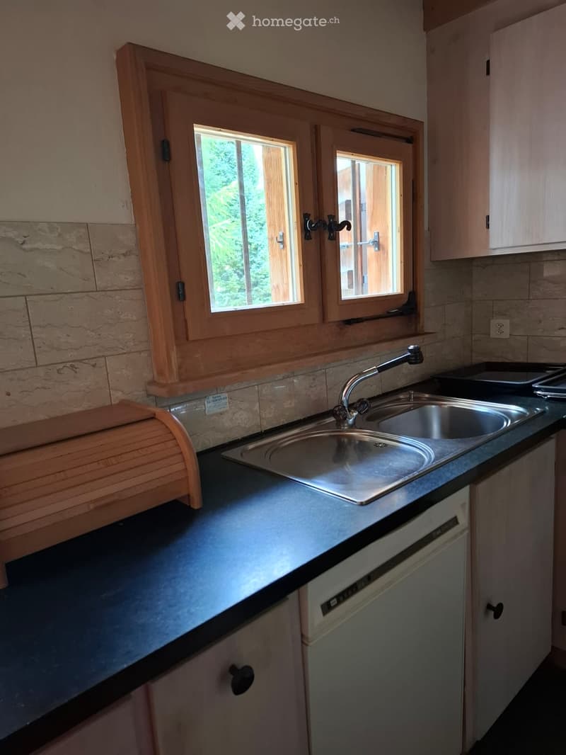 Kitchen with a double sink, faucet, dishwasher, and cabinets. The countertop is dark, and there is a window with wooden frames above the sink.