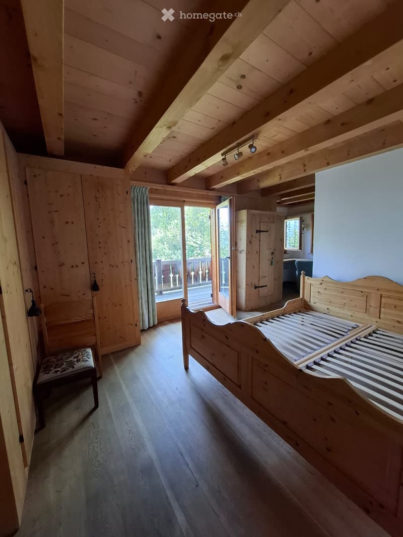 Cozy attic bedroom with wooden bed, exposed wooden beams, and a small balcony overlooking the outdoor deck.